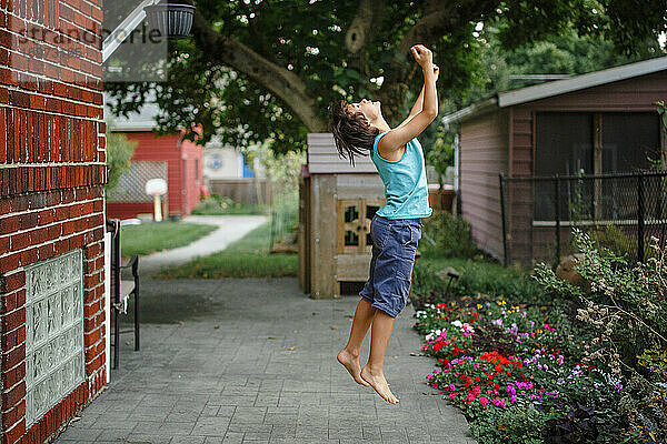 Ein kleiner Junge springt mit ausgestreckten Armen in die Luft in einem schönen Garten