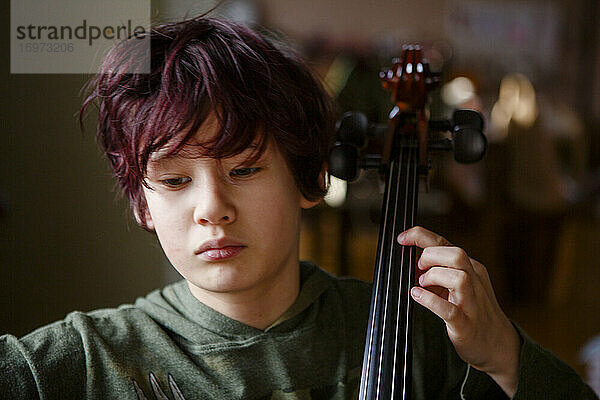 Nahaufnahme eines ernsten Jungen mit gefärbten roten Haaren beim Üben von Cellomusik