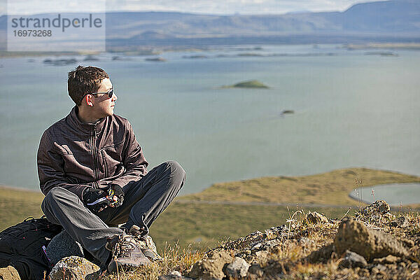 Jugendlicher  der sich auf dem Gipfel eines Berges über dem Myvatn-See in Island ausruht