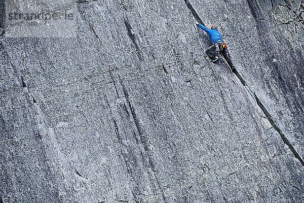 Mann klettert in einem Schiefersteinbruch in Nordwales eine steile Felswand hinauf