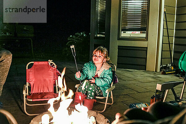 kleines Mädchen lächelnd vor einer Feuerstelle sitzend beim Essen