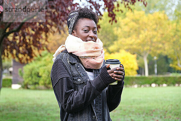 Schöne afrikanische Frau  die einen Schal trägt und eine Tasse Kaffee in einem Park hält. Herbst  Winter und kalte Konzepte.