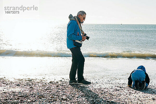Opa fotografiert seinen Enkel an einem sonnigen Tag am Strand