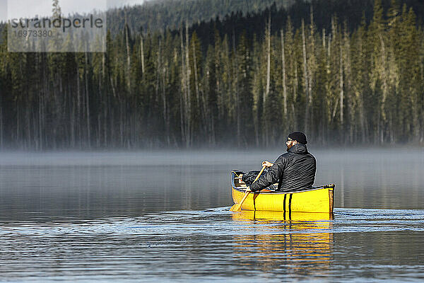 Bärtiger Abenteurer paddelt allein auf einem ruhigen  nebligen See in einem Kanu
