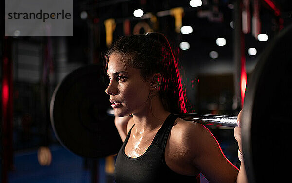 Verschwitzte Frau beim Training mit einer Langhantel im Fitnessstudio