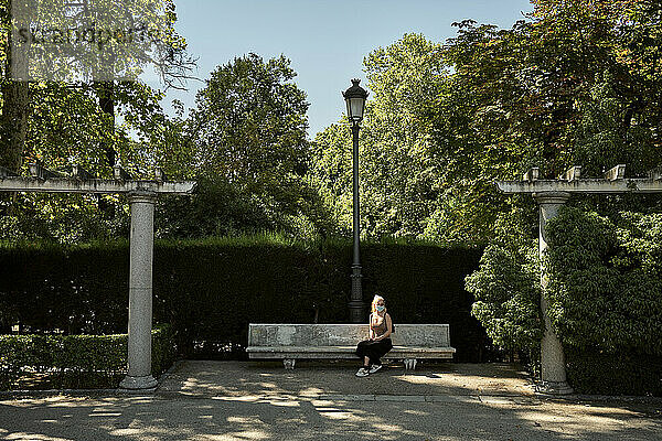 Frau mit Maske sitzt auf einer Bank im Park