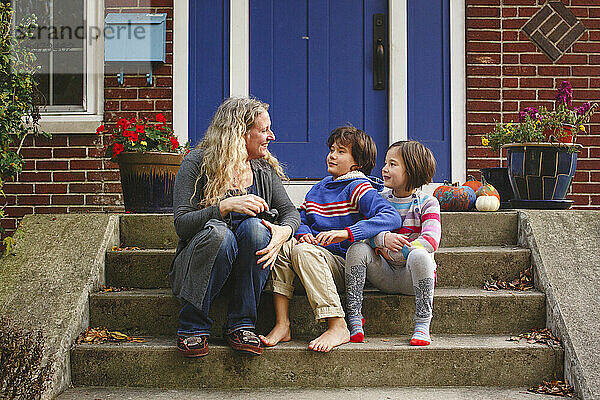 Eine lächelnde Mutter sitzt mit ihren beiden Kindern auf der vorderen Treppe ihres Hauses