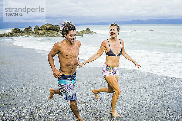 Multiethnisches Paar im Costa-Rica-Urlaub läuft am Strand