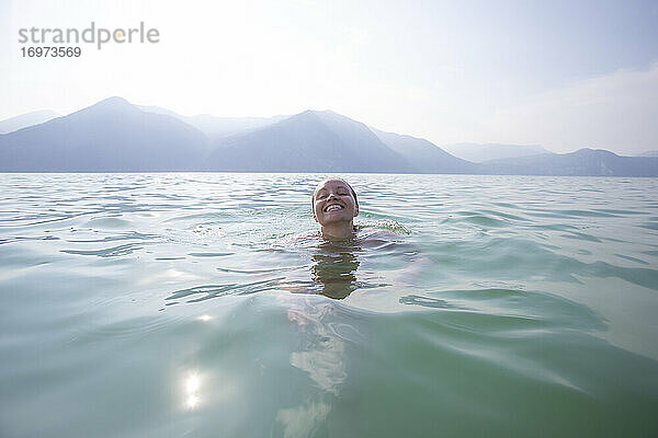 Eine lachende und lächelnde junge Frau  die in einem See in Italien schwimmt