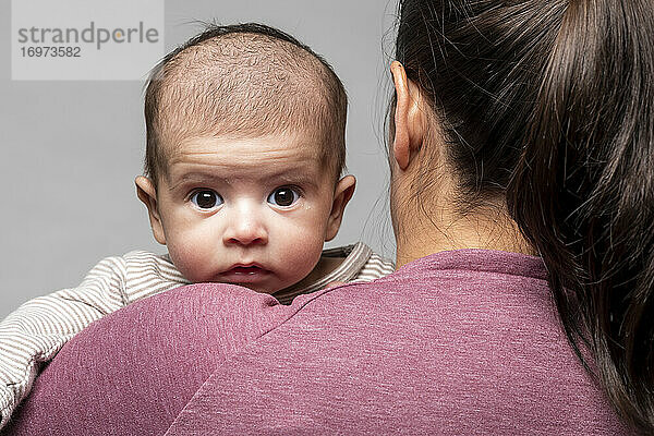 Ein Baby in den Armen seiner Mutter schaut ihr intensiv über die Schulter