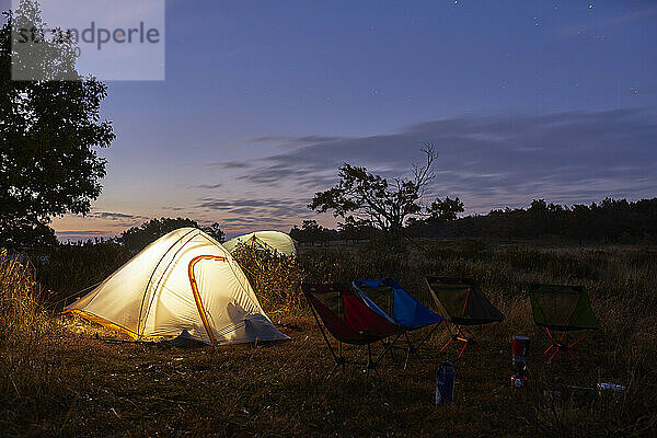 Beleuchtete Backpacker-Zelte auf einem Feld kurz vor Sonnenaufgang.