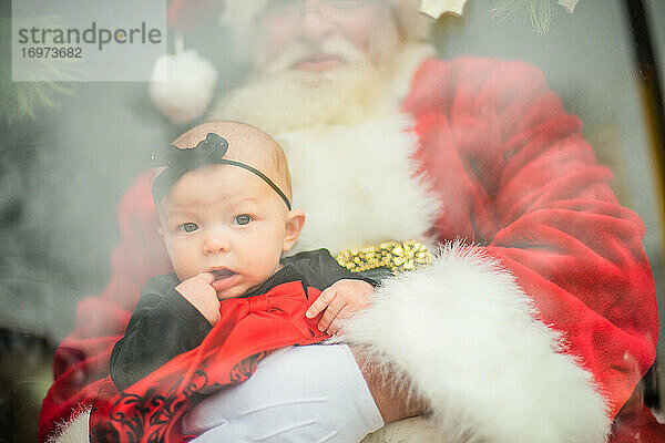 Baby sitzt auf dem Schoß des Weihnachtsmanns im Fenster