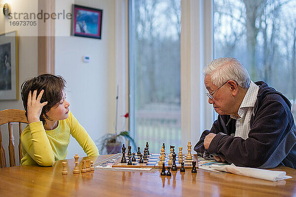 Ein Großvater studiert sorgfältig ein Schachbrett  während sein Enkel zuschaut
