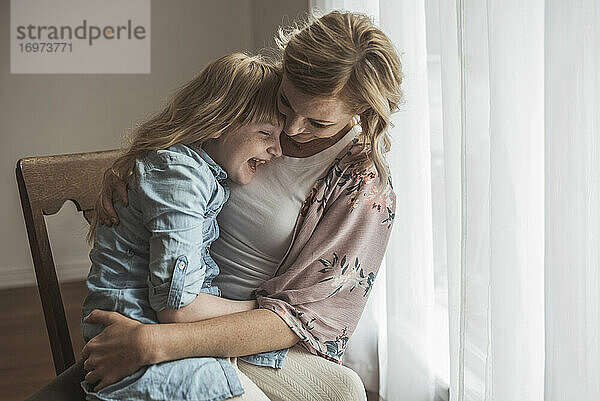 Mutter und Tochter lachen eng beieinander im Studio bei natürlichem Licht