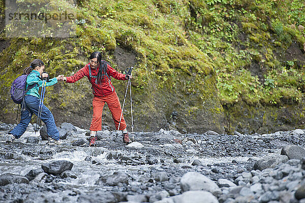 Mutter hilft ihrer Tochter beim Sprung über einen Fluss in Island