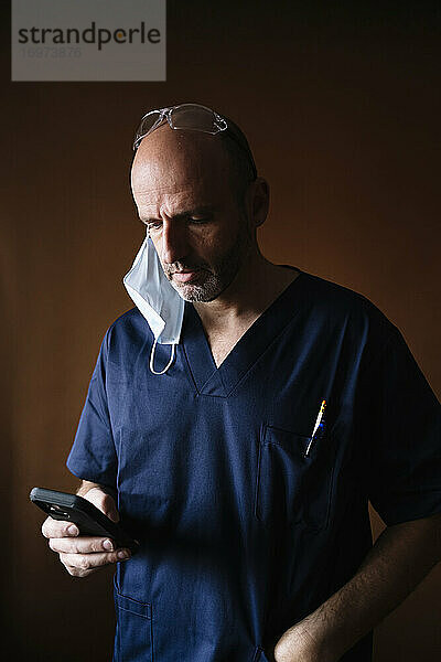 Porträt eines männlichen Arztes mittleren Alters  der ein Smartphone benutzt