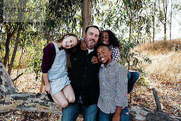 Papa & Kinder umarmen & lächeln für die Kamera im Park in Chula Vista