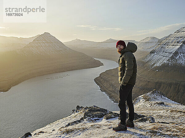 Mann auf verschneitem Berg mit Blick auf das Meer auf den Färöer Inseln