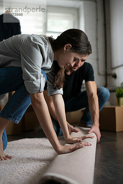 Junge Frau rollt mit Freund Teppich aus