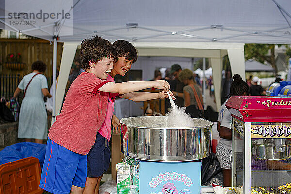 Zwei lächelnde Jungen machen gemeinsam Zuckerwatte auf einem Straßenfest im Sommer