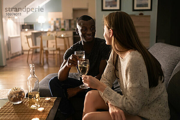 Fröhlicher schwarzer Mann trinkt Wein mit Freundin auf dem Sofa