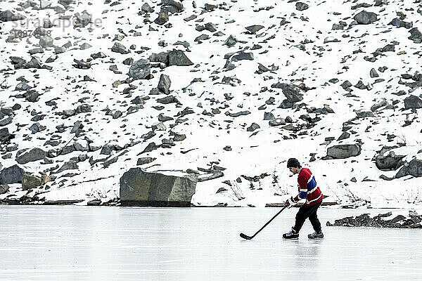 Mann spielt Eishockey in der Nähe eines verschneiten Berghangs in Kanada