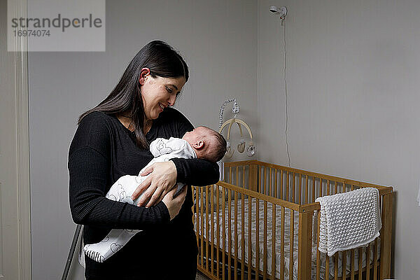Eine Mutter hält ihren neugeborenen Sohn in einem Kinderzimmer im Arm und schaut ihn an