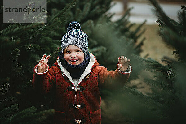 Junger Junge lächelnd zwischen Kiefern draußen an einem kalten Wintertag