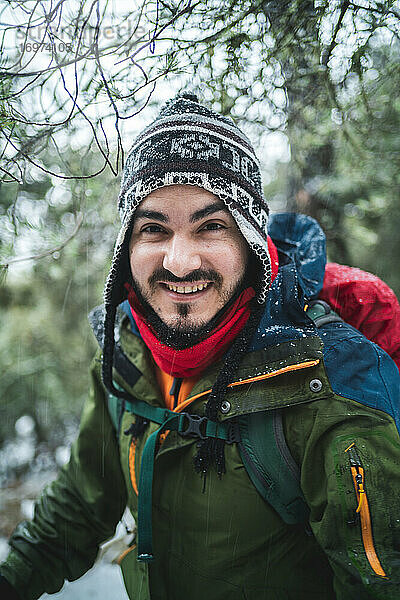 Mann lächelt in die Kamera mit Kälteschutz in einem verschneiten Wald