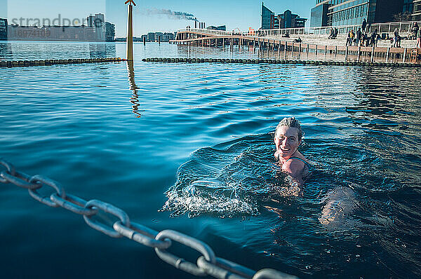 Lächelnde Frau schaut in die Kamera und schwimmt in kaltem Wasser in Dänemark