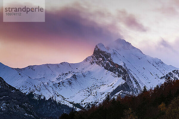 verschneiten Berg zwischen Wolken mit Bäumen bunte Blätter bei Sonnenuntergang