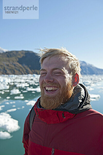 blonder Mann mit Bart lachend am Fjord in Südgrönland
