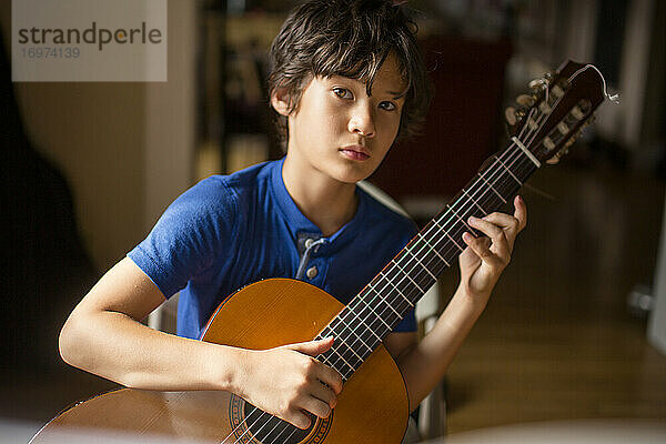 Ein Junge mit direktem Blick und ernster Miene hält eine klassische Gitarre