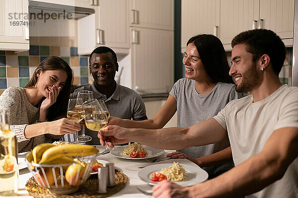Multiethnische Freunde stoßen beim Abendessen mit Weingläsern an