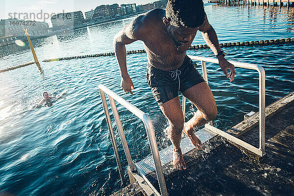 Junger multirassischer Mann  der nach dem Schwimmen in Dänemark aus dem kalten Wasser kommt