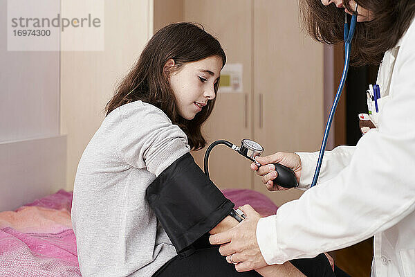 Ärztin  die den Druck auf den Arm eines Mädchens in ihrem Bett untersucht. Hausarzt-Konzept
