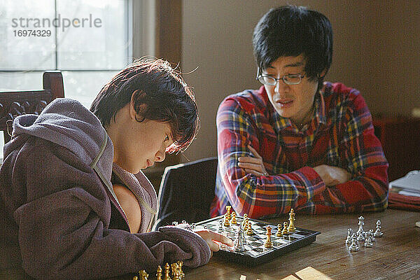 Ein Vater schaut zu  während ein kleiner Junge einen Schachzug im Schachspiel entscheidet