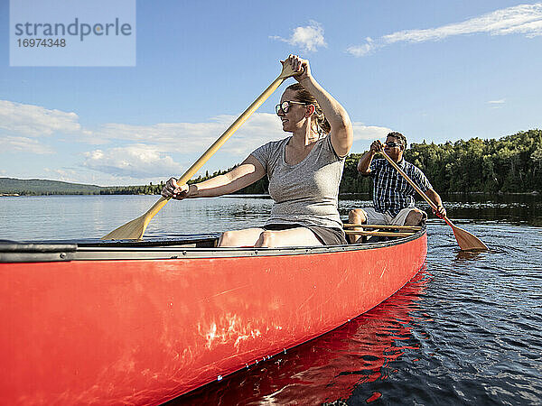 Glückliches mehrrassiges Paar paddelt mit einem roten Kanu auf einem unberührten See in Maine