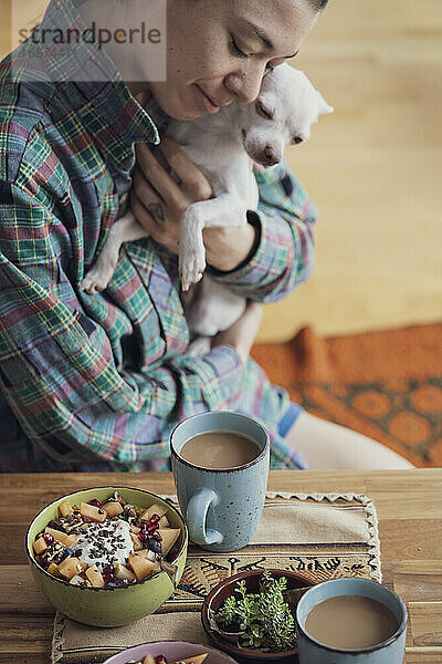 glücklicher Mensch kuschelt mit süßem Hund zu Hause bei Kaffee und Frühstück