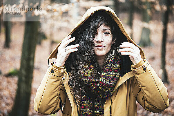 Junge Frau mit lockigem langem Haar lächelt im warmen Wintermantel im Wald