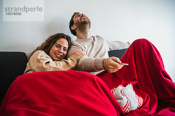 Fröhlicher Mann und Frau sehen mit Decke zugedeckt fern