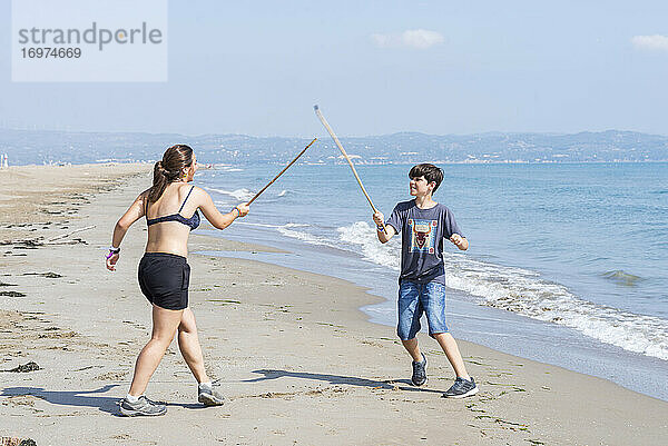 Zwei junge Freunde spielen mit Holzschwertern am Meeresstrand