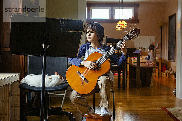 Ein Junge sitzt ruhig neben einer Katze  die Gitarre spielt  während seine Schwester dahinter sitzt