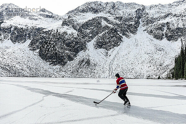Eishockeyspieler beim Schlittschuhlaufen auf einem zugefrorenen See in der Nähe eines verschneiten Berges