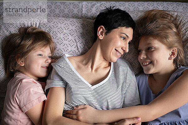 Glückliche Mutter umarmt Töchter im Bett am Morgen