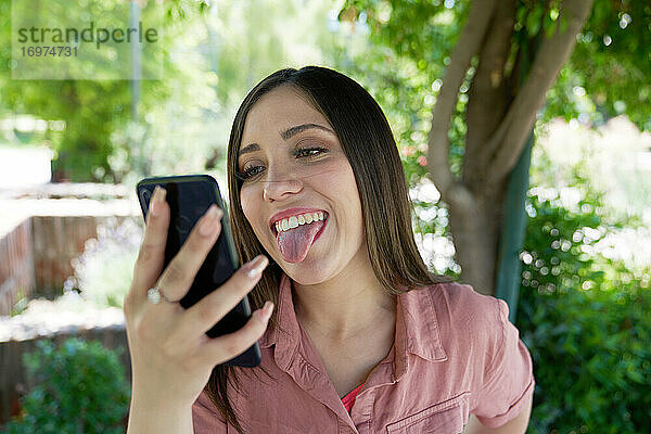 Eine schöne weiße Latina  die bei einem Videoanruf ihre Zunge herausstreckt