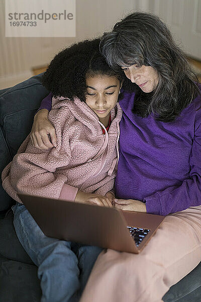 Kaukasische Mutter  gemischtrassige Tochter auf der Couch  die zusammen einen Film ansehen