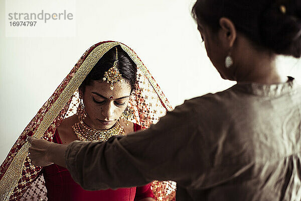 Junge Frauen helfen indischer Braut bei der Vorbereitung des traditionellen Kleides für die Hochzeit