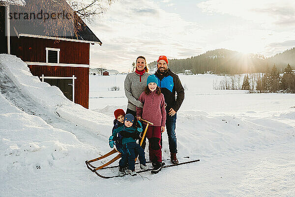 Glücklich lächelnde Familie in verschneiten Landschaft Bauernhof bei Sonnenuntergang