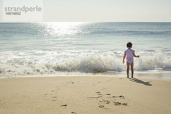 Ein kleines Mädchen steht am Rande des Ufers mit anrollender Welle